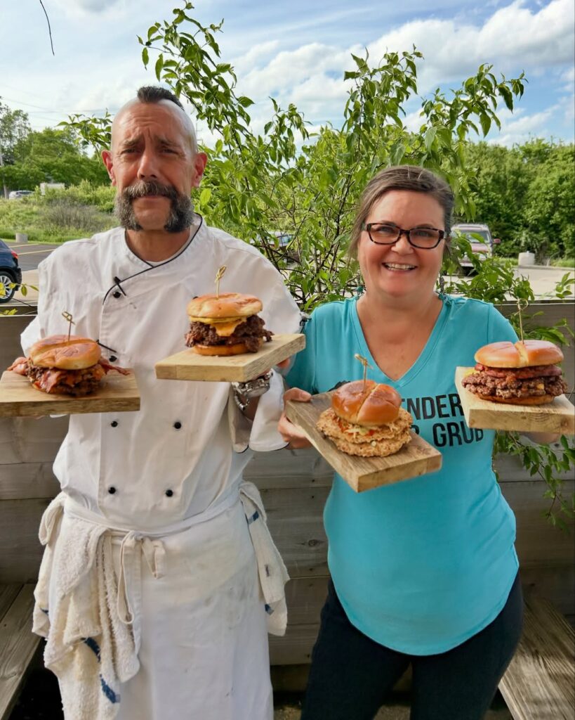 A photo of Chef Shawn Weinbender and Lora Damron holding up their award-winning smash burgers.