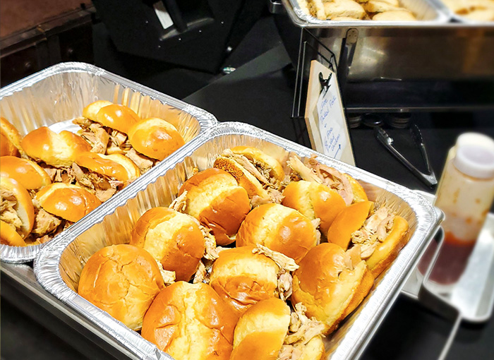 A photo of 19 pulled pork sliders next to a bottle of barbeque sauce.