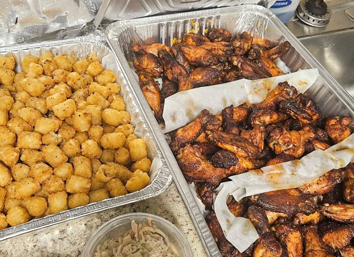 A photo of a catering spread with tater tots and smoked chicken wings.