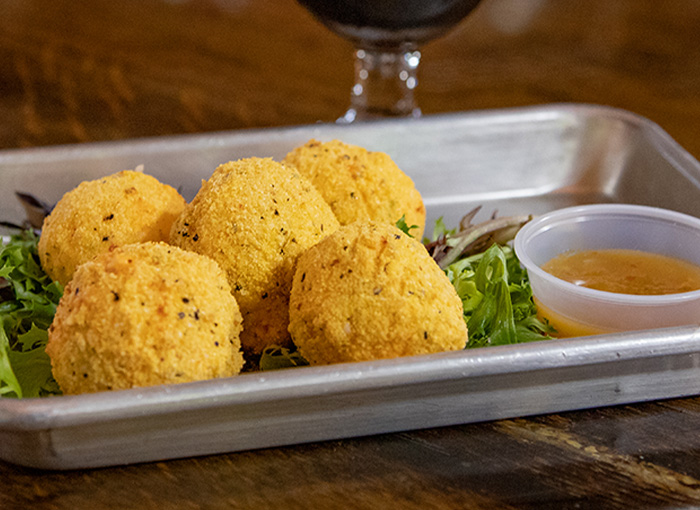 A photo of five fried cornmeal dusted pimento cheese fritters served next to a small container of green tomato jam.